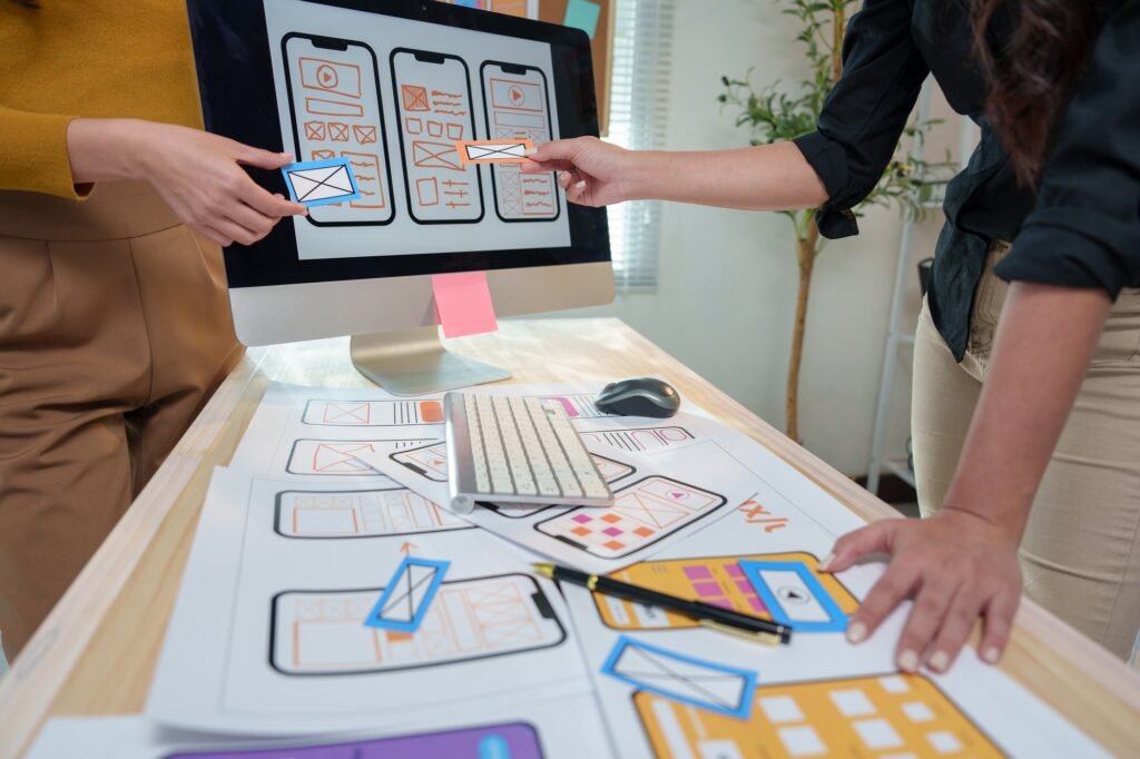 Two female web designers are discussing the user interface and user experience of a mobile app, comp